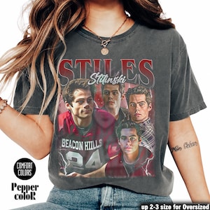 Op de afbeelding: Donkergrijs T-shirt met een afbeelding van een persoon en de tekst "STILES Stilinski" en "BEACON HILLS 24". Het shirt heeft de woorden "COMFORT COLORS" en "Pepper color" erop gedrukt. Het shirt is verkrijgbaar in 2-3 maten voor een oversized pasvorm.