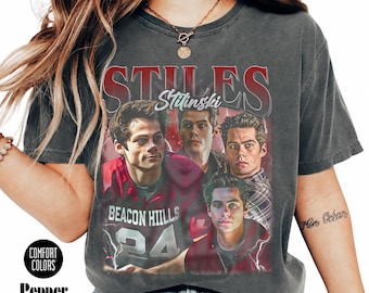 Puede incluir: Camiseta gris oscuro con un gráfico de una persona y el texto "STILES Stilinski" y "BEACON HILLS 24". La camiseta tiene las palabras "COMFORT COLORS" y "Pepper color" impresas. La camiseta está disponible en tallas de 2-3 para un ajuste oversize.
