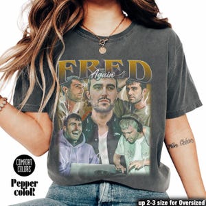 May include: A dark gray Comfort Colors t-shirt featuring a collage of images of a man with the text "FRED Again" in gold lettering. The shirt also has the words "Pepper color" printed on it.