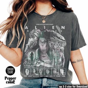 May include: Dark grey t-shirt featuring a movie poster design for "Alien: Romulus." The graphic includes images of characters and the text "Alien Romulus" and "In space, no one can hear you." The shirt is from Comfort Colors.