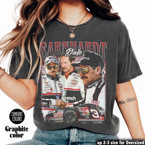 May include: A charcoal gray short-sleeve t-shirt featuring a graphic print of Dale Earnhardt. The design includes three portraits of the driver wearing racing gear and sunglasses, the text EARNHARDT Dale, and a black number 3 race car at the bottom.