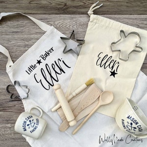 May include: A baking set for children with a white apron, a canvas bag, a mug, a rolling pin, a wooden spoon, a spatula, a pastry brush, and cookie cutters. The apron and bag are personalised with the name "Elleri" and the text "Little Baker".