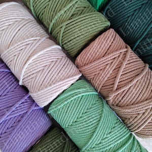 May include: A collection of colorful macrame cords in various shades of green, beige, and purple. The cords are tightly wound into neat bundles, showcasing their texture and color variations. Ideal for crafting and DIY projects.