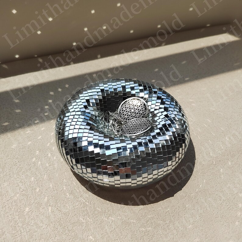 May include: A silver mirrored disco ball shaped trinket dish with a silver geometric design pendant resting inside.