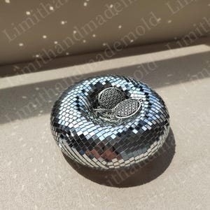 May include: A silver disco ball shaped trinket dish with two silver earrings with a geometric design inside.