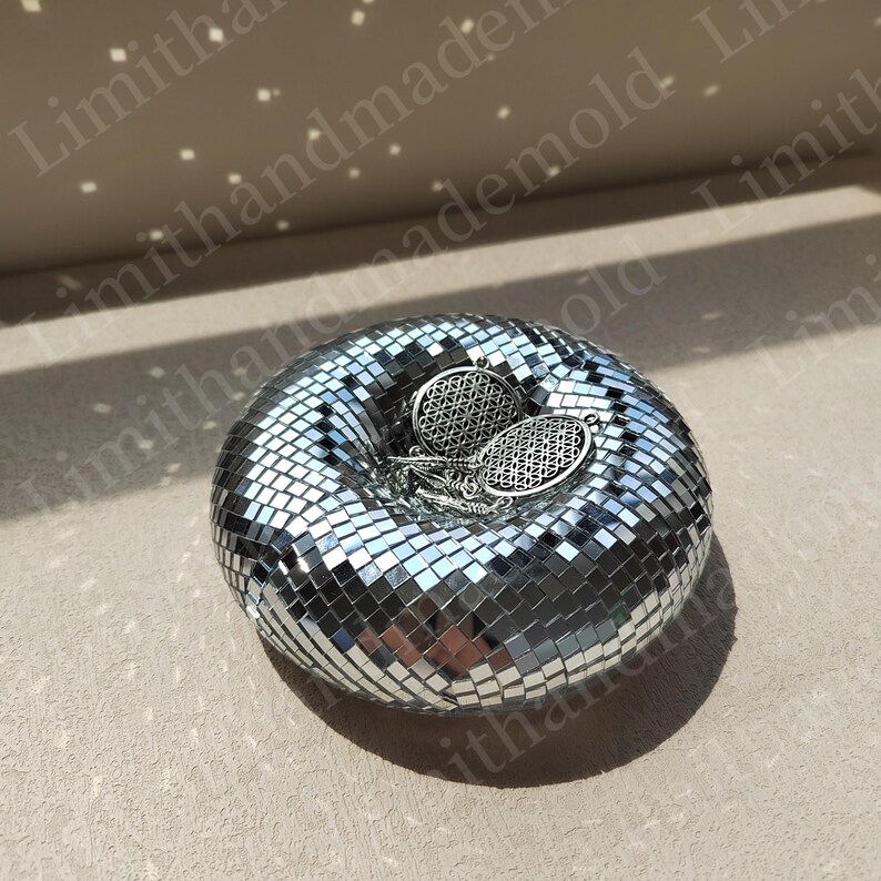 May include: A silver disco ball shaped trinket dish with two silver earrings with a geometric design inside.