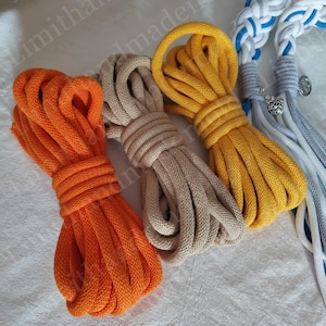 May include: Three spools of cotton rope in orange, beige, and yellow. The rope is thick and has a soft texture.