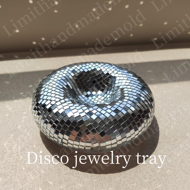 May include: A silver disco ball shaped jewelry tray. The tray is made of small mirrored tiles and has a deep center.