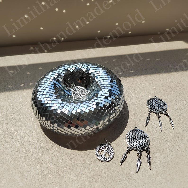 May include: A silver mirrored mosaic bowl with a silver metal charm inside. Three silver metal charms with feathers hang on the right side of the bowl.