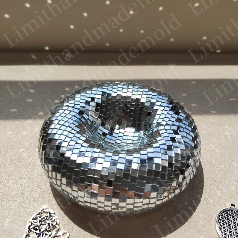 May include: A silver disco ball shaped like a donut with a hole in the center. The ball is made of small, mirrored tiles.