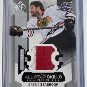 Peut inclure: Une carte de hockey avec Brent Seabrook des Blackhawks de Chicago. La carte comprend un patch de maillot et le texte "2015 All-Star Skills Fabrics". La carte est dans une pochette de protection.