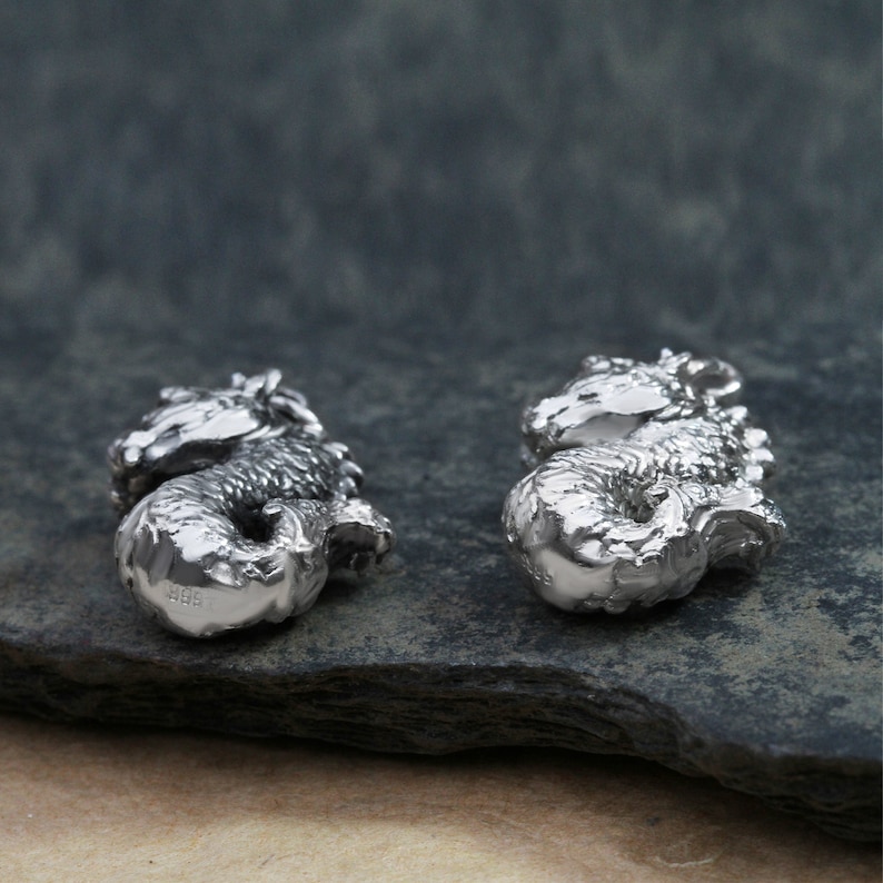 May include: Two silver seahorse charms, each with a detailed, textured design. The seahorses are facing opposite directions and are positioned on a gray, textured surface.