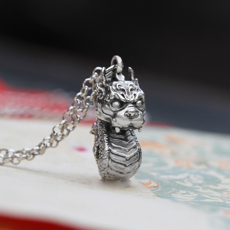 May include: A silver dragon pendant necklace. The dragon is detailed with scales and has a fierce expression. The necklace is made of a silver chain.