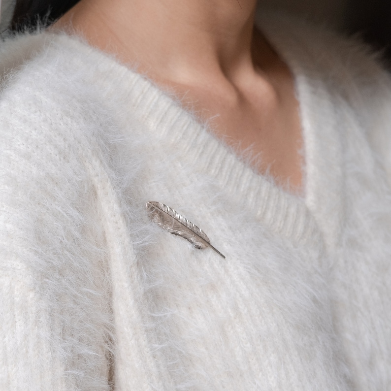 May include: A silver feather pin on a white fuzzy sweater.
