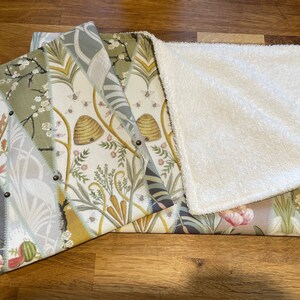 Peut inclure: Une couverture r&eacute;versible pour b&eacute;b&eacute; avec un motif botanique. Un c&ocirc;t&eacute; pr&eacute;sente un patchwork de tissus &agrave; motifs floraux et naturels avec des abeilles, des &eacute;cureuils et des fleurs. L'autre c&ocirc;t&eacute; est en mati&egrave;re pelucheuse blanche et douce. La couverture est pli&eacute;e, r&eacute;v&eacute;lant les deux c&ocirc;t&eacute;s.