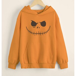 May include: Orange hoodie with a black and white pumpkin face graphic. The hoodie has a kangaroo pocket and a drawstring hood.
