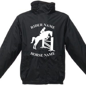 May include: Black equestrian jacket with a high collar and long sleeves. The jacket features a white graphic of a horse and rider jumping a fence, with the text "RIDER NAME" above and "HORSE NAME" below the graphic.