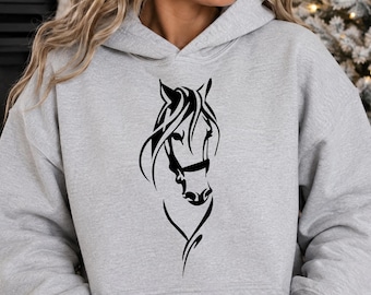 Puede incluir: Una sudadera con capucha de color gris claro que presenta un estampado gráfico negro de una cabeza de caballo en la parte delantera. La prenda incluye capucha con cordones, mangas largas y un bolsillo canguro frontal.