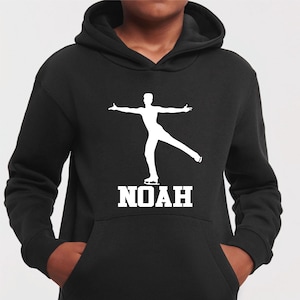 Puede incluir: Sudadera con capucha negra con un gráfico blanco de un patinador artístico en movimiento. El nombre "NOAH" está impreso en blanco debajo. La sudadera tiene un bolsillo de canguro.
