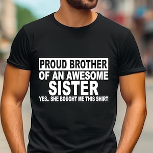 Peut inclure: Un t-shirt noir à manches courtes et col rond avec le texte blanc suivant : PROUD BROTHER OF AN AWESOME SISTER YES.. SHE BOUGHT ME THIS SHIRT. Le vêtement présente une coupe standard avec un col rond et un tissu noir uni sur toute la surface.