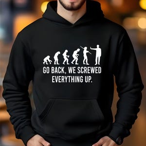 May include: A black hooded sweatshirt featuring a white graphic of human evolution ending with a figure holding a hand up in a stop gesture. Below the graphic, the text reads: GO BACK, WE SCREWED EVERYTHING UP. The hoodie has long sleeves and a front pocket.