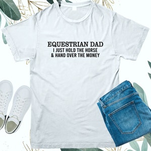 May include: White t-shirt with black text that reads "Equestrian Dad I just hold the horse & hand over the money"