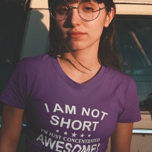 Puede incluir: Una camiseta morada con cuello en V con el texto "I AM NOT SHORT I'M JUST CONCENTRATED AWESOME!" en blanco. La camiseta la lleva una persona con gafas y pelo oscuro.