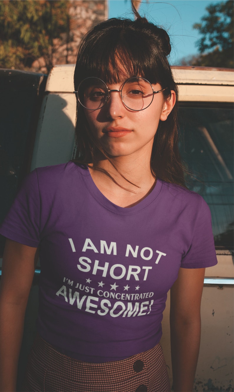 Puede incluir: Una camiseta morada con cuello en V con el texto "I AM NOT SHORT I'M JUST CONCENTRATED AWESOME!" en blanco. La camiseta la lleva una persona con gafas y pelo oscuro.