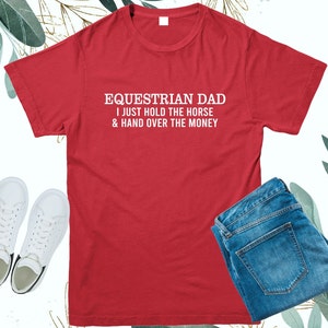 May include: Red t-shirt with white text that reads "Equestrian Dad I just hold the horse & hand over the money".