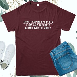 May include: Burgundy t-shirt with white text that reads "Equestrian Dad I just hold the horse & hand over the money"