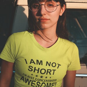 Puede incluir: Una persona con una camiseta verde lima con el texto "I AM NOT SHORT I'M JUST CONCENTRATED AWESOME!" en negro. La persona lleva gafas redondas y tiene el pelo oscuro.