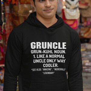 May include: Black hoodie with the word "GRUNCLE" in large white letters. The text below defines "GRUNCLE" as a cooler uncle. The hoodie has a front pocket and a drawstring hood.