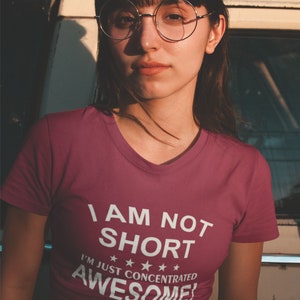 Puede incluir: Camiseta burdeos con cuello en V con el texto blanco "I AM NOT SHORT I'M JUST CONCENTRATED AWESOME!". La persona lleva gafas redondas.