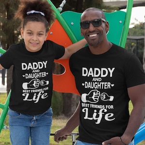 May include: Black t-shirts with white text reading "DADDY and DAUGHTER Best Friends for Life." A father and daughter wear the shirts. The daughter is in blue jeans. The father is wearing sunglasses.