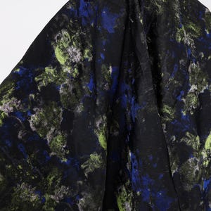 May include: Black fabric with a watercolor-style pattern. The design features splashes of blue, green, and white against a dark background. The fabric is draped, showing folds and texture.