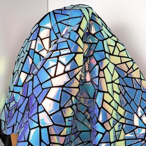 May include: Iridescent fabric with a geometric mosaic pattern in shades of blue, green, and yellow, outlined in black. The fabric has a shiny, reflective surface, creating a stained-glass effect. The material is draped over an unseen form.