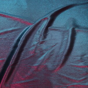 May include: A teal and burgundy iridescent fabric with a subtle shimmer. The fabric is wrinkled and has a textured surface.
