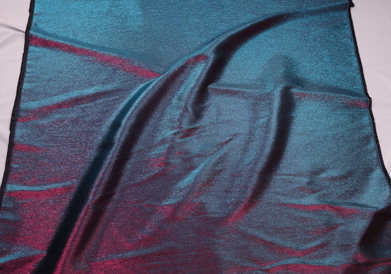 May include: A teal and burgundy iridescent fabric with a subtle shimmer. The fabric is wrinkled and has a textured surface.