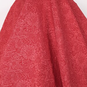 Puede incluir: Una tela roja vibrante con un patrón floral detallado. El diseño presenta una impresión total de flores y hojas, creando una apariencia texturizada. La tela está drapeada, mostrando su flujo y el intrincado diseño.