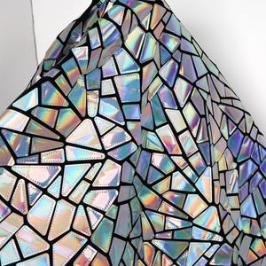 Può includere: Tessuto iridescente con un motivo geometrico a mosaico. Il tessuto presenta un retro nero con forme riflettenti multicolori. Le forme sono delineate da cuciture nere, creando un effetto vetrata. Il tessuto ha un aspetto lucido e olografico.