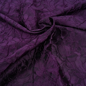 Peut inclure: Gros plan sur un tissu violet foncé avec un motif floral. Le tissu est texturé avec des motifs floraux en relief, créant un effet tridimensionnel. Les plis et les ombres ajoutent de la profondeur à la couleur riche et sombre.