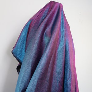 May include: A shimmering iridescent fabric with a blue and purple gradient. The fabric is draped over a white surface.