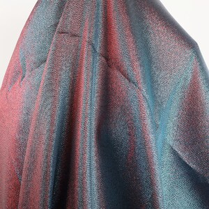 May include: Close-up of iridescent fabric with a blue and pink color gradient. The fabric has a textured, shimmering surface.