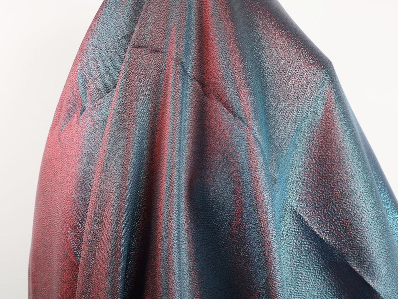 May include: Close-up of iridescent fabric with a blue and pink color gradient. The fabric has a textured, shimmering surface.