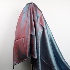 May include: A shimmering iridescent fabric with a blue and pink color gradient. The fabric is draped over a mannequin and has a subtle sparkle.