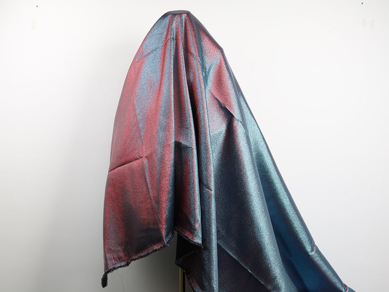 May include: A shimmering iridescent fabric with a blue and pink color gradient. The fabric is draped over a mannequin and has a subtle sparkle.