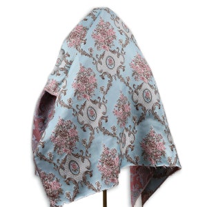 May include: A light blue fabric with a floral pattern. The fabric has a damask design with pink and brown flowers and a white background. The fabric is draped over a stand.