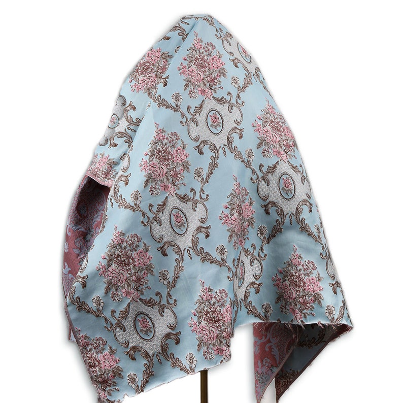 May include: A light blue fabric with a floral pattern. The fabric has a damask design with pink and brown flowers and a white background. The fabric is draped over a stand.