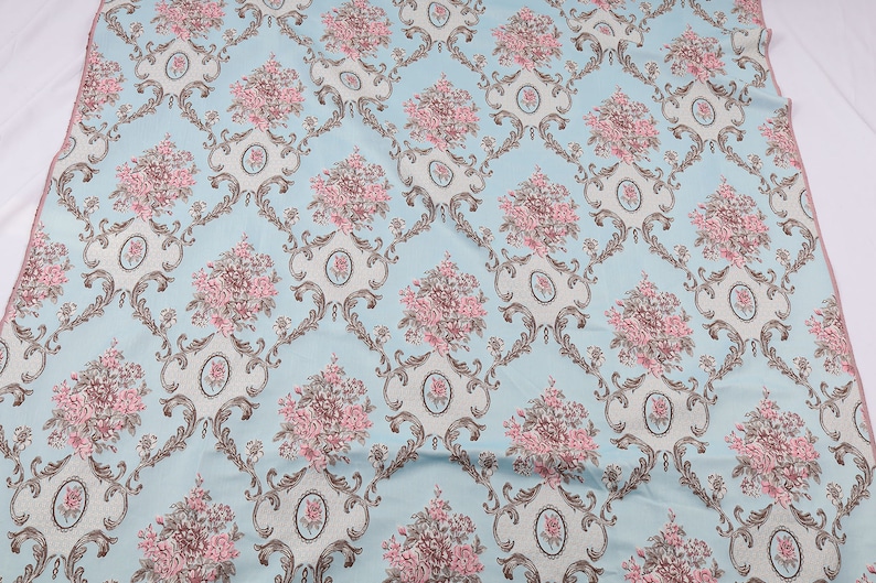 May include: A light blue fabric with a repeating pattern of pink and brown floral bouquets in ornate frames.