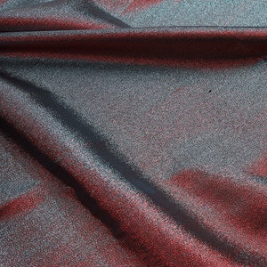 May include: Close-up of a shimmering fabric with a red and silver color gradient. The fabric is folded and draped, creating soft folds and wrinkles.